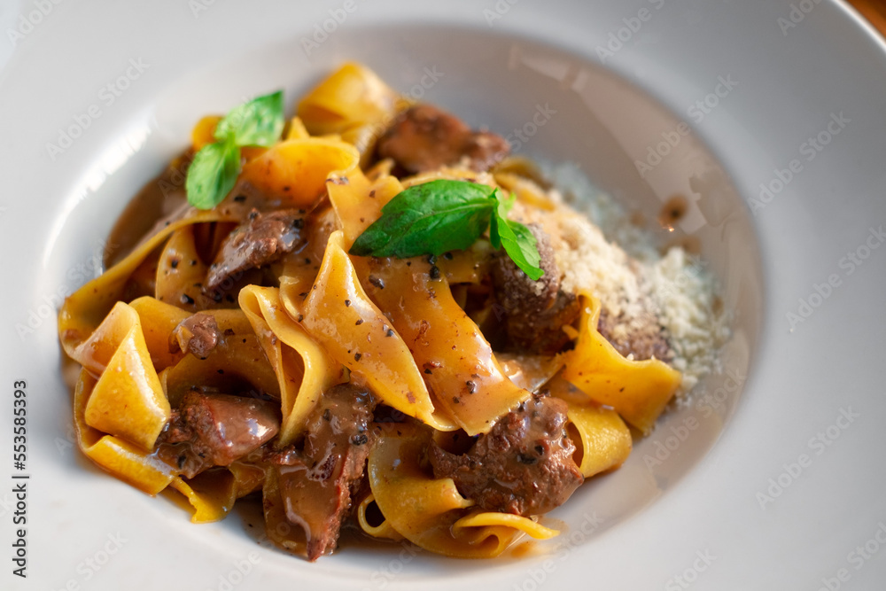 Papardelle pasta with beef, gravy, parmesan and basil on a white plate. Italian dish served Papardelle pasta with beef, gravy, parmesan and basil on a white plate. Italian dish served