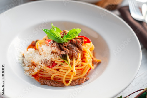 Spaghetti pasta with tomato sauce and beef stew, tomatoes, parmesan cheese and fresh basil on a wooden background. Italian cuisine