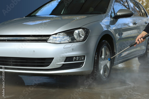 Man washing auto with high pressure water jet at outdoor car wash, closeup