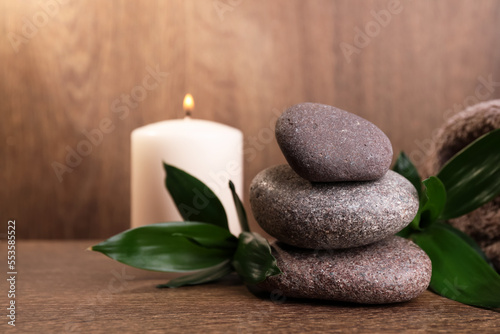 Stacked spa stones, bamboo leaves and candle on wooden table. Space for text