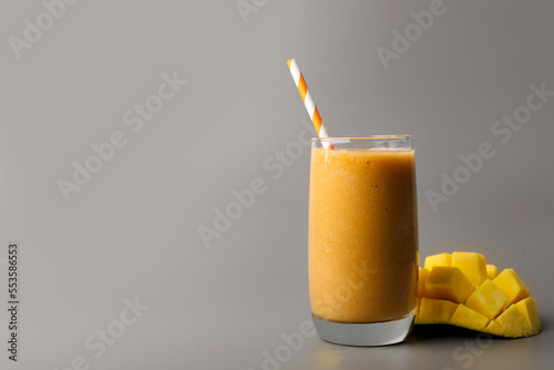Glass with delicious fresh fruit smoothie and mango on grey background. Space for text