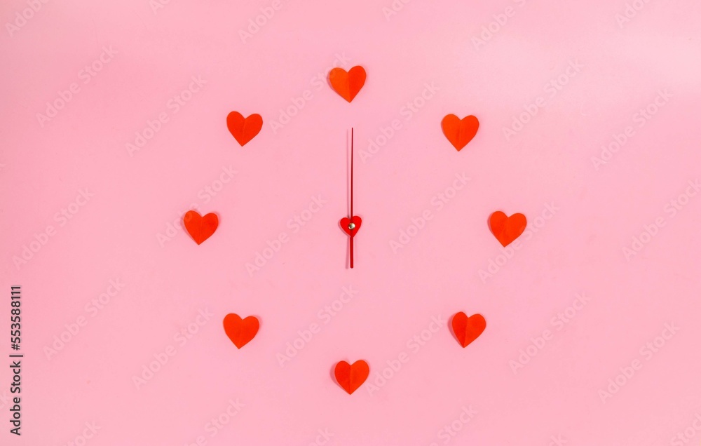 Clock hands in the center of a circle of red paper hearts. Love time.