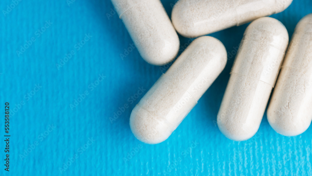 White pills, medicine capsules, vitamins or drugs on blue background, medication treatment, health care concept White pills, medicine capsules, vitamins or drugs on blue background, medication treatment, health care concept