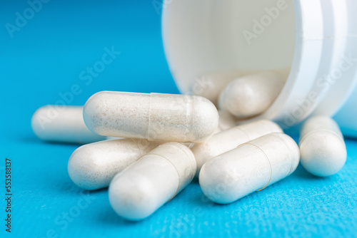 White pills, medicine capsules, vitamins or drugs on blue background, medication treatment, health care concept