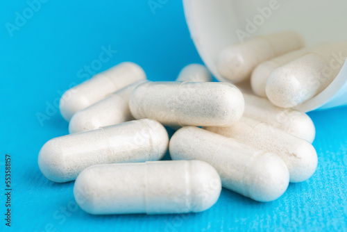 White pills, medicine capsules, vitamins or drugs on blue background, medication treatment, health care concept