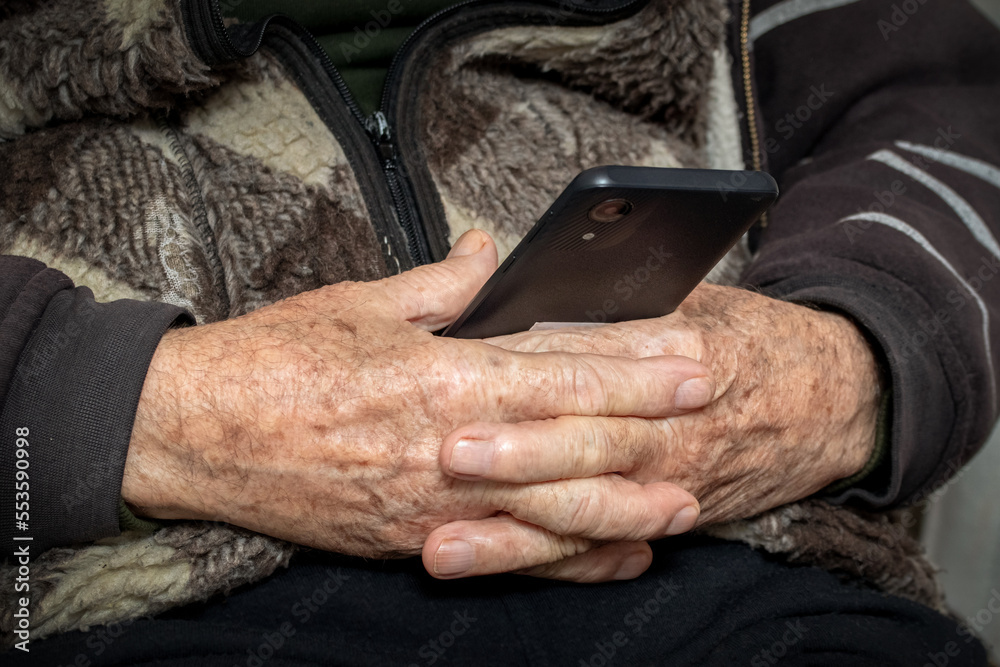 Grandfather holds a mobile phone in his hands. Leisure for the elderly