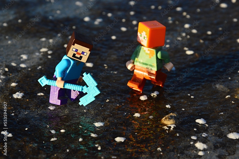 Obraz premium LEGO Minecraft figures of Steve and Alex trying to break thick layer of real ice on a lake with diamond pickaxe.