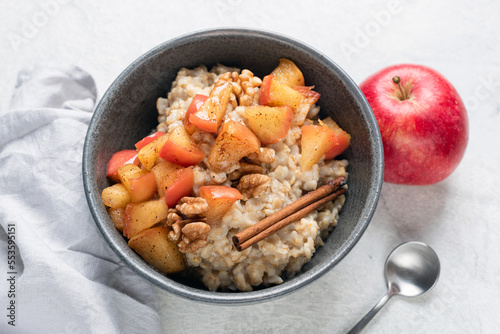 Oatmea porridge with red apple, walnuts and cinnamon in a bowl, closeup view. Healthy vegan breakfast, autumn comfort food