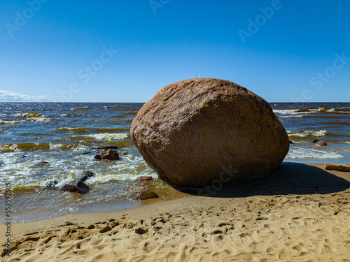 Beautiful seascape. Reflection of sunlight on sea waves. Huge stone on sandy beach.