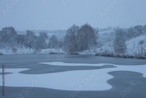 Winter landscape with frozen river and snow covered trees on hill  © Juver