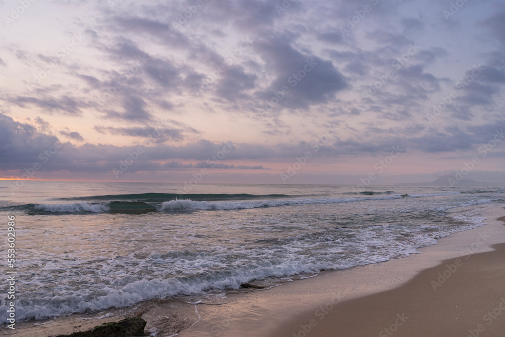 Spectacular sunrise on the beach of Gandia with pink and orange sky and rocks near the water. Spain