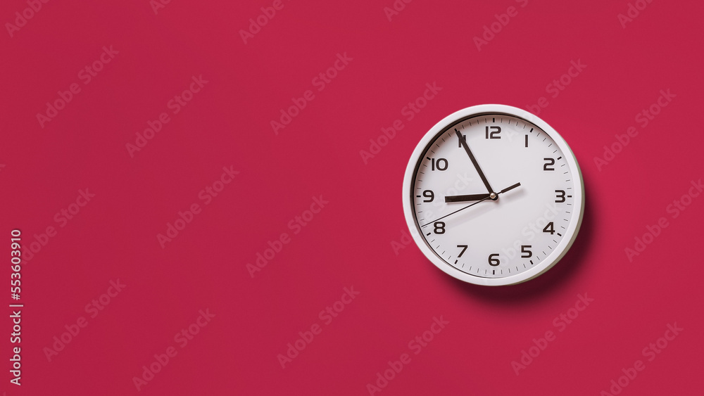 Wall clock over viva magenta background. Round white clock with black hands. Five minutes to nine. Time measuring, hour and minutes concepts. Color of the year 2023. Copy space. Wall clock over viva magenta background. Round white clock with black hands. Five minutes to nine. Time measuring, hour and minutes concepts. Color of the year 2023. Copy space.