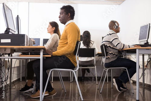 Portrait of positive young adult man studying in computer class at library