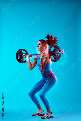 Studio shot of a female bodybuilder lifting barbell. Long exposure movement capture.