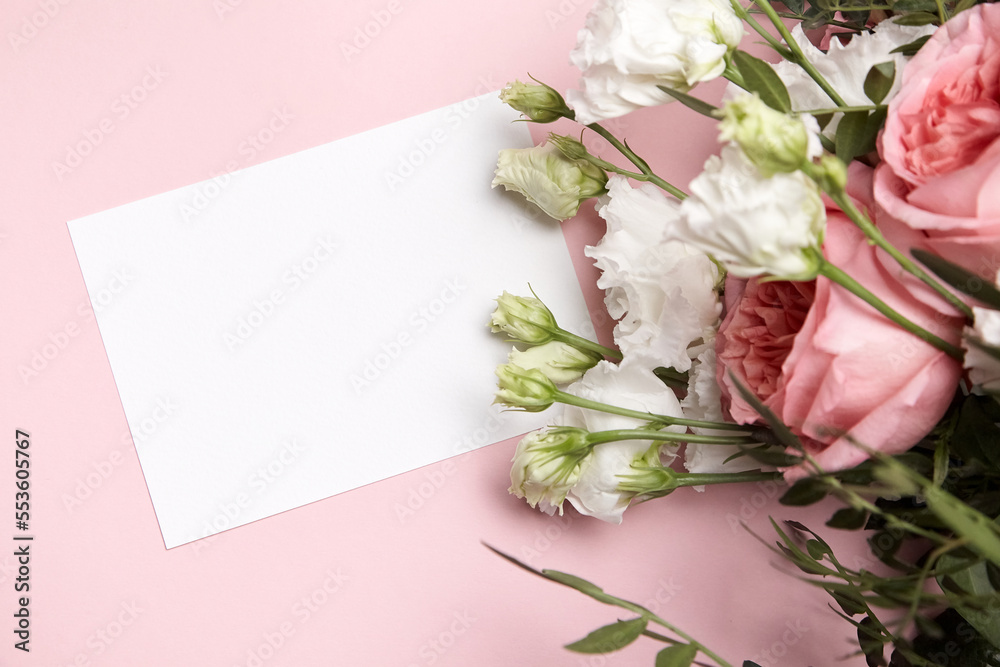 Holiday greeting card mockup with flowers on light pink background, top view, flat lay. White wedding invitation mockup and floral decor