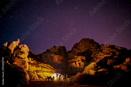A group by a campfire that lights up granite rocks under a starlit sky. photo