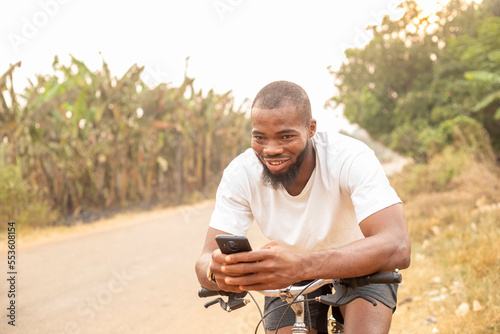 copy space of young black man smiling using phone while sitting on bicycle