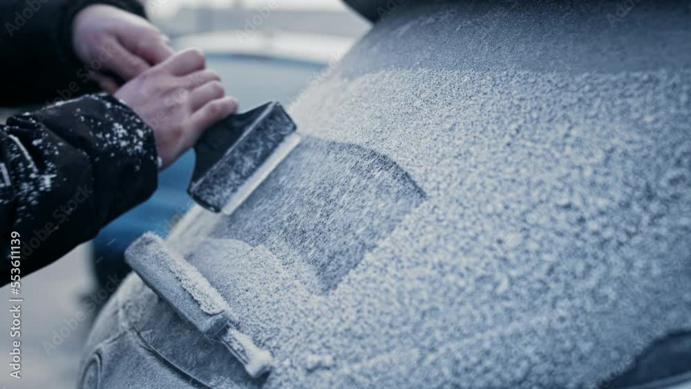 A man in a winter coat uses an ice scraper to remove heavy frost and ice from the windows and windshield of a frozen car on a sub-zero Winter morning. A man in a winter coat uses an ice scraper to remove heavy frost and ice from the windows and windshield of a frozen car on a sub-zero Winter morning.