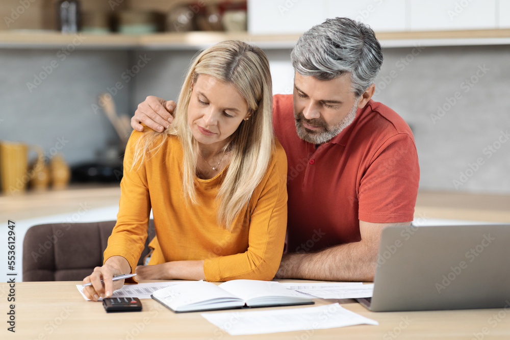 Mature spouses sitting at kitchen desk in front of computer Mature spouses sitting at kitchen desk in front of computer