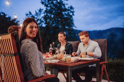 A group of young diverse people having dinner on the terrace of a modern house in the evening. Fun for friends and family. Celebration of holidays  weddings with barbecue.