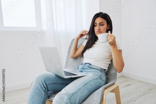 Woman relaxing at home sitting in a chair and watching a movie on her laptop with a cup of tea, fall mood, freelancer lifestyle