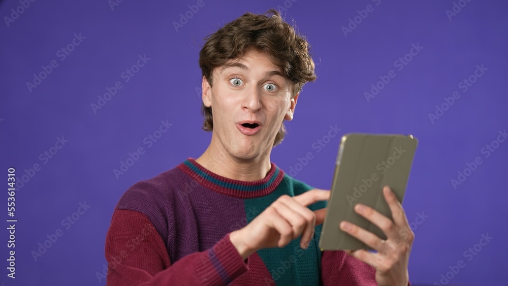 Portrait of happy smiling young guy 20s in sweater shopping on tablet computer point with finger give thumbs up isolated on purple background studio. Portrait of happy smiling young guy 20s in sweater shopping on tablet computer point with finger give thumbs up isolated on purple background studio.