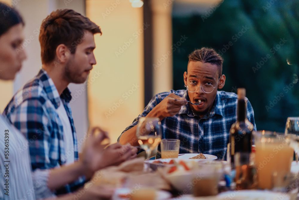 A group of young diverse people having dinner on the terrace of a modern house in the evening. Fun for friends and family. Celebration of holidays, weddings with barbecue.