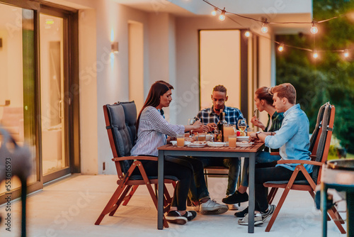 A group of young diverse people having dinner on the terrace of a modern house in the evening. Fun for friends and family. Celebration of holidays  weddings with barbecue.