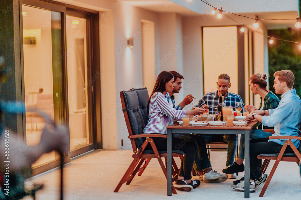 A group of young diverse people having dinner on the terrace of a modern house in the evening. Fun for friends and family. Celebration of holidays, weddings with barbecue. A group of young diverse people having dinner on the terrace of a modern house in the evening. Fun for friends and family. Celebration of holidays, weddings with barbecue.