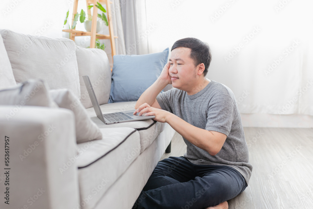 Asian man sitting on floor and do work with laptop computer, he work from home and search information, internet and network technology Asian man sitting on floor and do work with laptop computer, he work from home and search information, internet and network technology