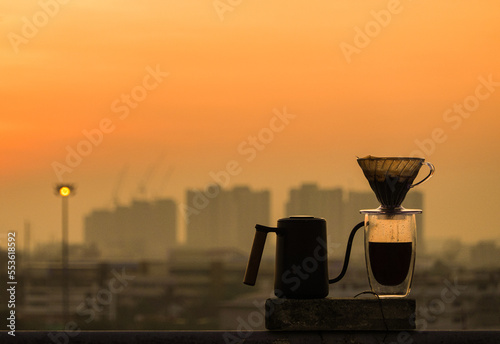 A cup of drip coffee on the table with a sunrise city view background.