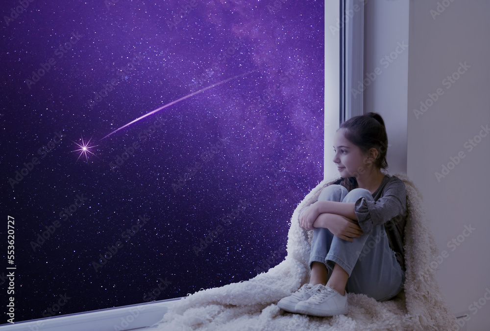 Cute little girl sitting on windowsill and looking at shooting star in ...