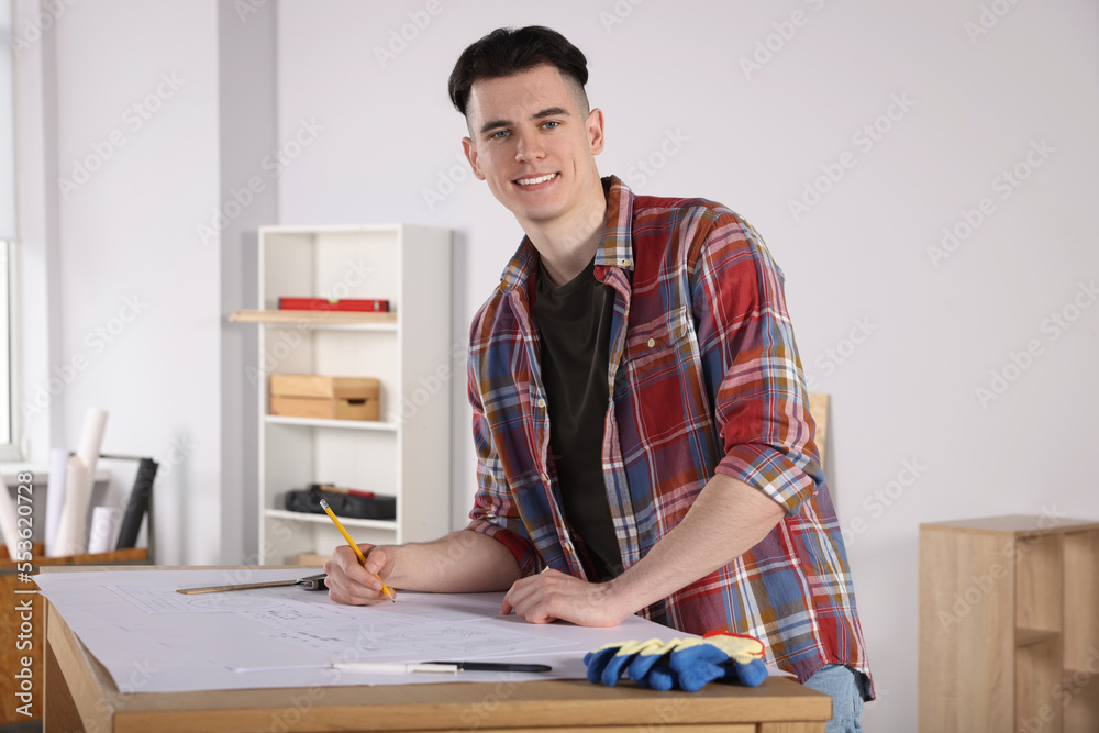 Young handyman working with blueprints at table in room Young handyman working with blueprints at table in room