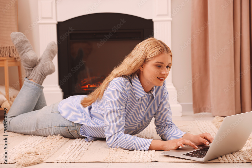 Young woman working on laptop near fireplace in room Young woman working on laptop near fireplace in room