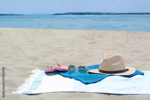 Blanket with towel, flip flops, hat and sunglasses on sandy beach near sea, space for text