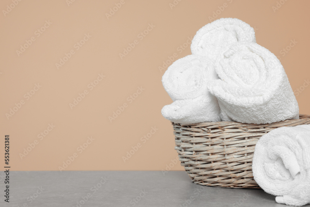 Fototapeta premium Soft rolled towels in wicker basket on grey table, space for text