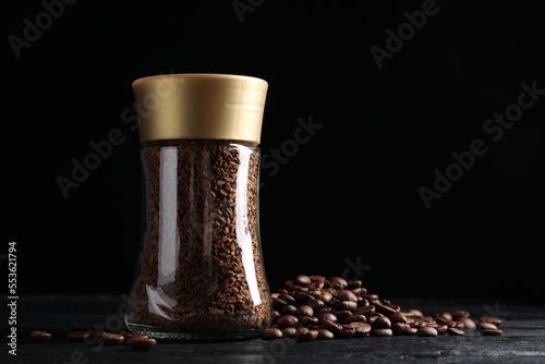 Glass jar with aromatic instant coffee and beans on black wooden table. Space for text