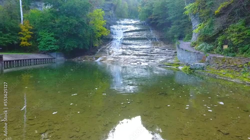 Aerial over hiking bridge viewing huge cascading waterfall over rocks in forest park of New York Aerial over hiking bridge viewing huge cascading waterfall over rocks in forest park of New York