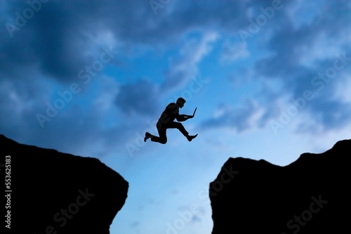 Silhouette of business man jumping on rock