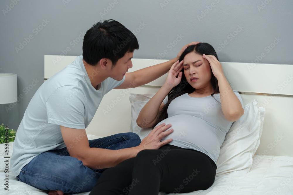 pregnant woman having headache with her husband on bed pregnant woman having headache with her husband on bed
