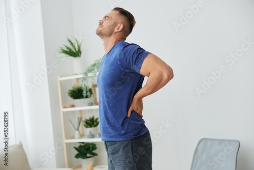 Man backache neck and shoulder pain, inflammation of muscles and ligaments rupture during sports, inflammation and injury, in a blue t-shirt at home