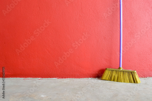 Plastic broom laid against the red wall. Copy space for the text.