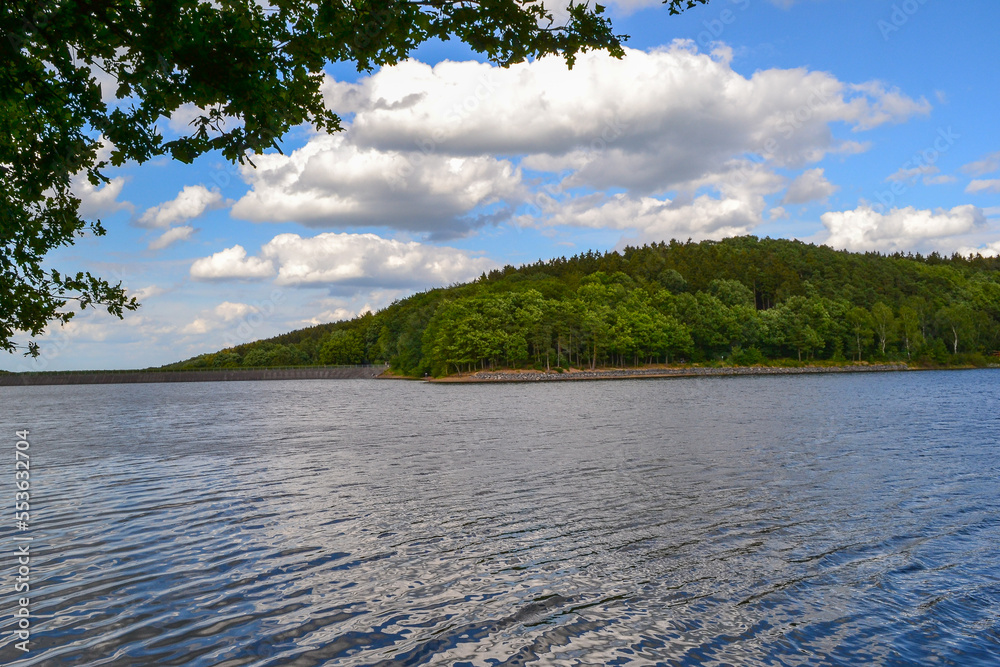 A lake at a dam with a forest and clouds in the sky.