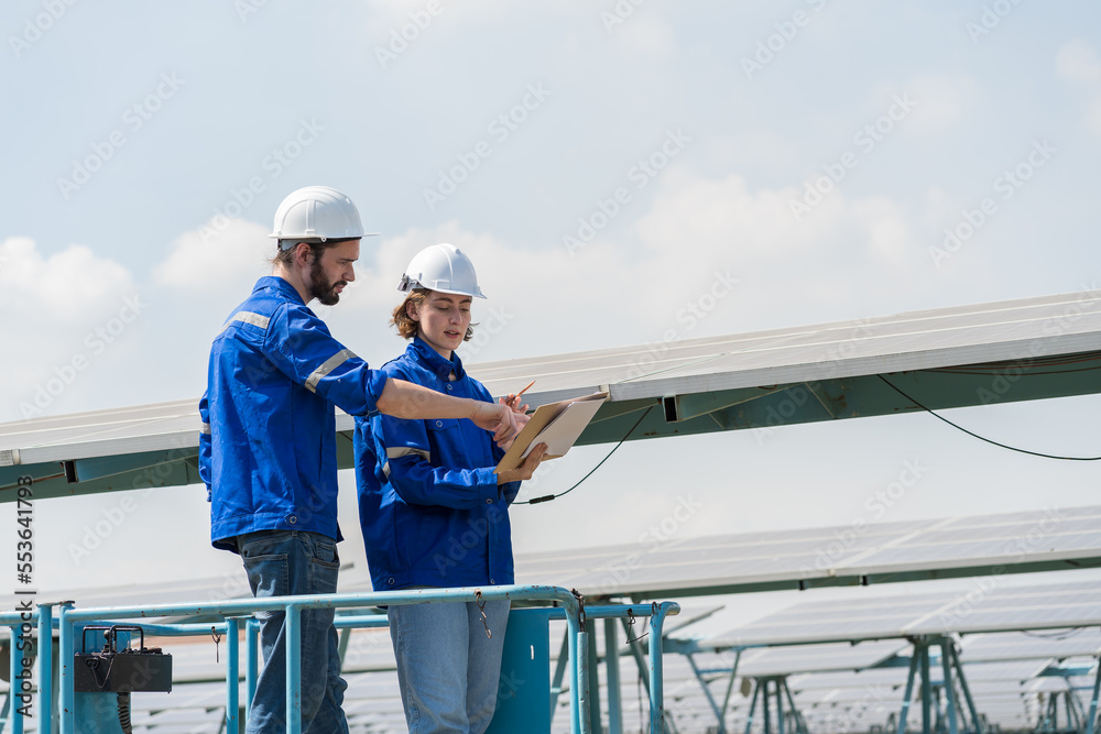 Two male and female electrician worker on forklift truck working in solar panels power farm between long rows array of photovoltaic solar cells panels