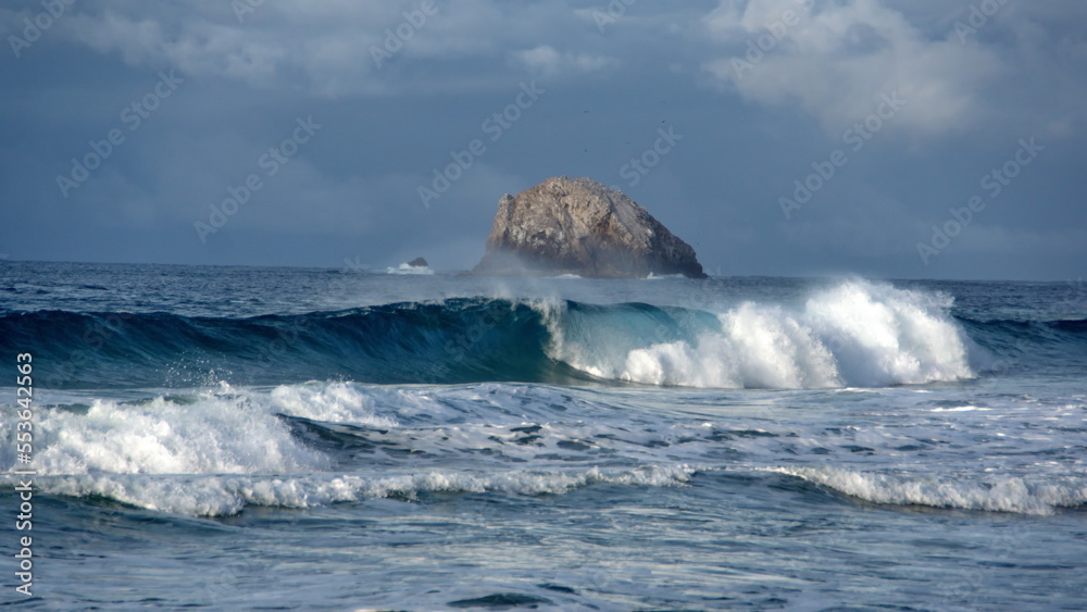 Waves breaking on the beach, with a rocky islet in the background, in the morning in Zipolite, Mexico