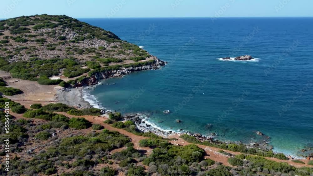 Shore of Crete Island with waves hitting the beach surrounded by forest and trails, blue sky Shore of Crete Island with waves hitting the beach surrounded by forest and trails, blue sky