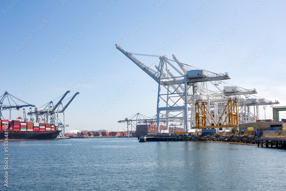 A view of a port terminal where large cranes unload shipping containers from a cargo ship.