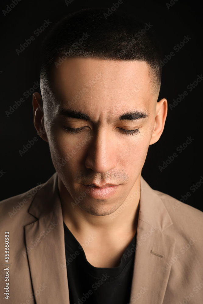 Young Asian man with closed eyes on black background