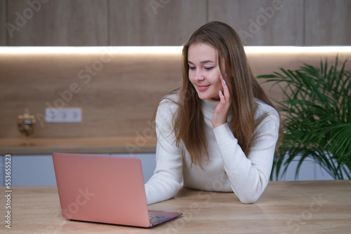 beautiful girl, young woman freelancer is using laptop computer at home at kitchen, freelace distant job photo