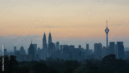 Time lapse: Silhouette of KL cityscape view during golden dawn overlooking the city skyline from afar with yolk sun & lushes green in the foreground. Kuala Lumpur, Malaysia.  Prores 4KUHD timelapse.